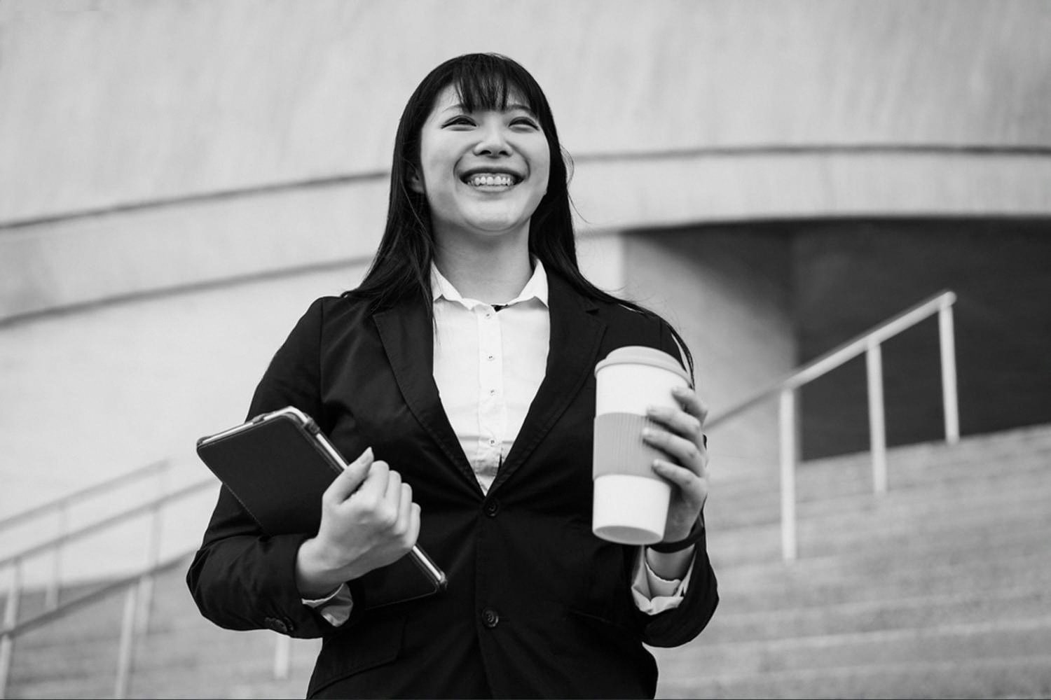 Smiling new employee holding a tablet and coffee cup outside a UAE corporate building on her first day